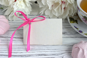 Peonies flowers pink cup of tea greeting card marshmallow on a white wooden background - stock image.