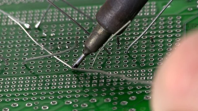 An electrical engineer builds a circuit design by soldering through hole components to a breadboard by hand