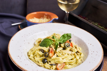Pasta with chicken, olives and cheese on ceramic plate with glass of white wine