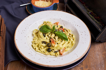 Pasta with chicken, olives and cheese on ceramic plate with glass of white wine on wooden table in rustic style.