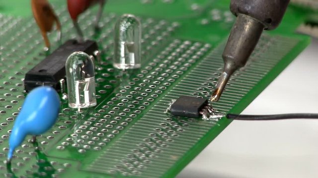 An electrical engineer builds a circuit design by soldering a wire to a surface mount IC pin on a breadboard