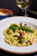 Closeup view of Pasta with chicken, olives and cheese on ceramic white plate with glass of white wine on table