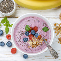 Healthy delicious smoothie from banana and fresh berries raspberry and blueberry granola with Chia seeds and mint leaves in white bowl