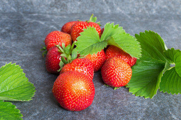 Strawberries and green leaves on a black stone