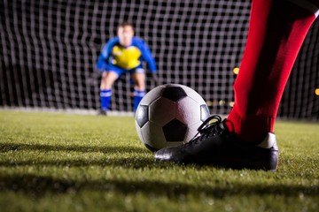 Low section of soccer player with ball against goalkeeper