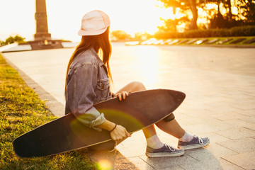 Young girl with longboard in the park at sunrise or sunset