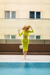 Beautiful woman in big hat posing next to the pool.