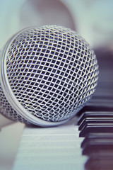 Close up on a microphone during recording session with a singer, piano in the background, music studio.