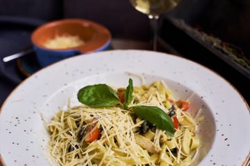 Traditional italian pasta served on table in rustic style. Tagliatelle with chicken slices, olives and cheese.