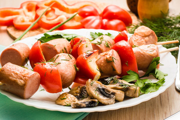 Fried sausage with peppers on skewers and mushrooms on a plate