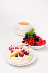 Meringue cake with strawberries, raspberry, peach, black currant, cherry and cream. A porcelain saucer with fresh fruits and cup of coffee  in the background. Shallow depth of field