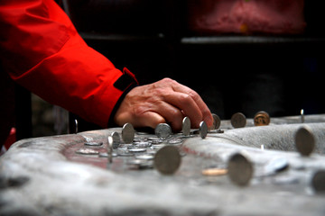 Man making coin stand on its side on a stone