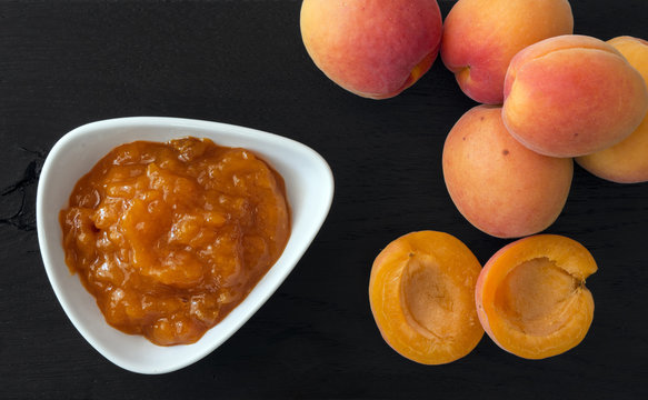 Apricot jam and apricots arranged on black wooden background