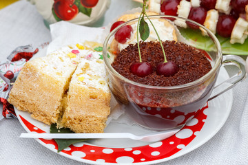 A big piece of cake and drink with grated chocolate and cherries on a white plate is represented at the village festive fair dedicated to the harvest of cherries.