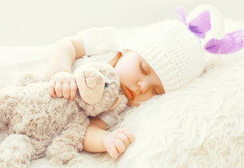 Cute baby sleeping with teddy bear toy on a white soft bed at home