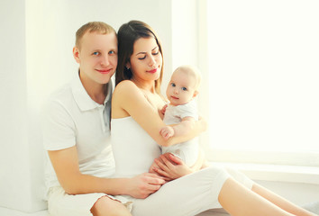 Fototapeta na wymiar Happy family together, mother and father with baby home in white room near window