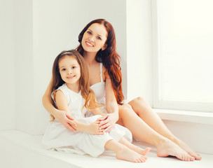 Obraz na płótnie Canvas Happy smiling mother and daughter child together at home in white room sitting near window