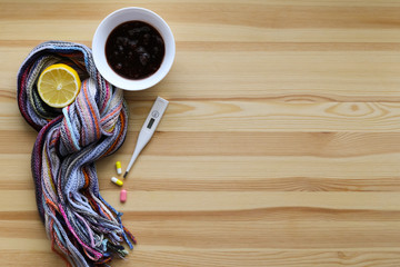 Treatment for cold and throat pain. Thermometer, jam, lemon and tablets on the light wooden background