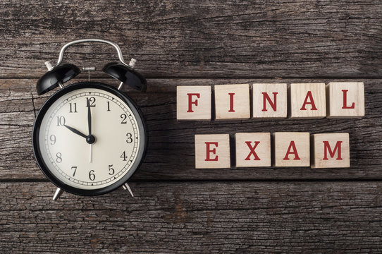 "Fianl exam" text on wood block with the alarm clock on the wood background.