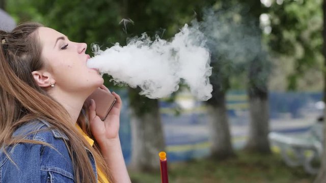 woman pull hookah and talking on cell phone in parkland, beautiful girl holding shisha pipe outdoors, lovely female inhale taste tobacco on vacation, young women smoking hookah in open air