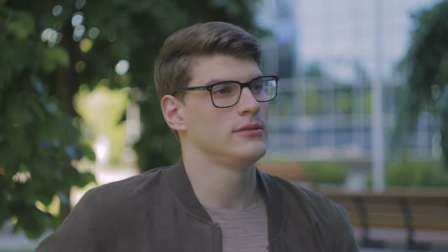 Young attractive man in glasses, in park on bench, smoking a cigarette