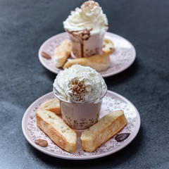Two cups with hot chocolate garnish, whipped cream, cocoa powder, toasts, leaves of bitter chocolate