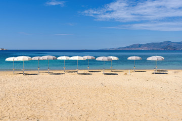 Fototapeta na wymiar White parasols on Idyllic tropical beach with sand, turquoise sea water and blue sky. Naxos island. Cyclades, Greece. 