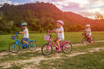 Obraz premium Three child riding a bicycle. The kids in a helmet riding a bike in the park. Beautiful kids.