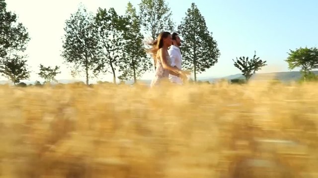 Teenage girlfriend and boyfriend having fun and running outdoors / A couple   in love in the middle of nature holding hands smiling in sunset light in a wheat field / slow-mo / 720p / steady-cam