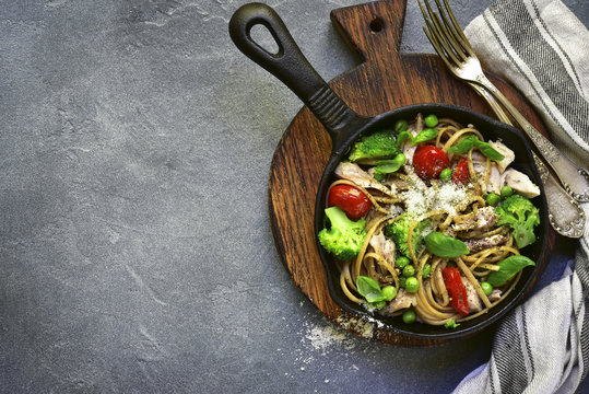 Whole wheat pasta with chicken fillet and vegetables in a cast iron  pan.Top view with space for text.