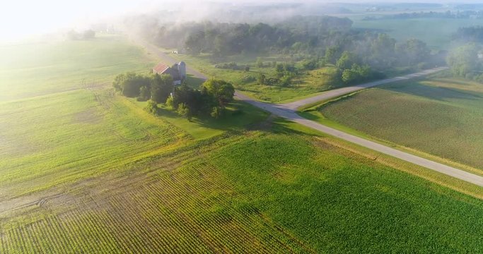 Breathtaking aerial view of farms and fields amid foggy sunrise.
