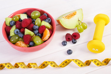 Fruit salad and centimeter with dumbbells, healthy lifestyle, food and nutrition