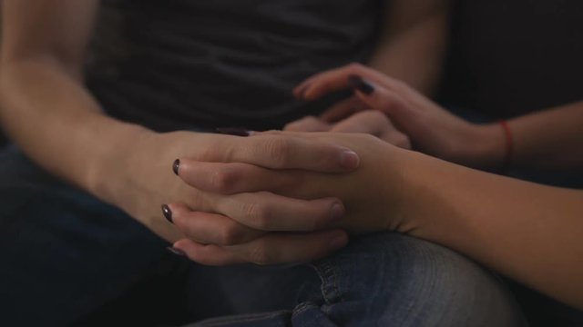 Close up view of couple hands, sitting on sofa at home in the living room.