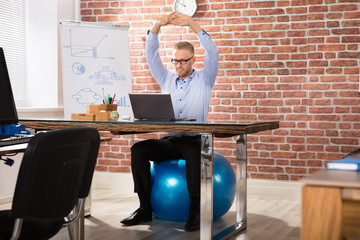 Happy Businessman Relaxing On Fitness Ball In Office