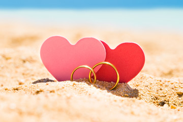 Fototapeta premium Two Heart Shapes With Golden Rings On Sand
