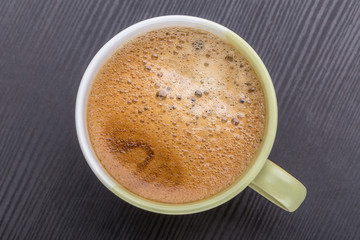 Hot black coffee with foaming in green cup placed on dark wooden table, morning coffee concept.