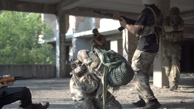 Two men in uniform attacking terrorists and freeing hostage inside of ruined building.