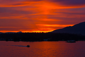 Scarlet sunset over the city of Vancouver, BC, Canada. Mountains landscape during sunset with water and high pine trees on horizon.