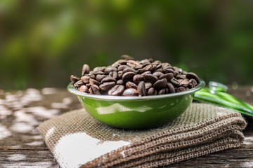 Coffee beans in green bowl on old wood background with sunlight