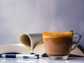 A cup of hot coffee, Cappuccino, with a reading book, on a table in the Morning, vintage style background