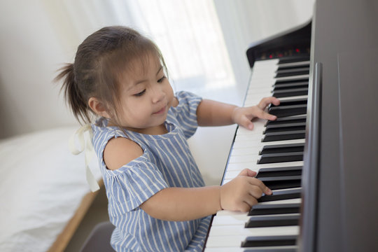 Happy little Asian girl playing piano at home
