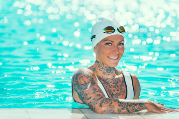 Portrait of female swimmer with tattoos on pool edge