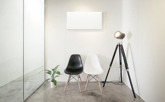 Empty office waiting room.Loft interior style , white canvas print on the center white wall. Two black and white chairs at the concrete floor .