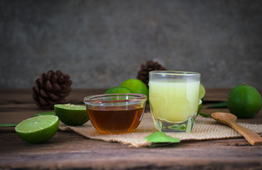 a Lime lemon with juice  and honey in transparent glass with sack cloth on rustic wooden background. copy space for graphic designer
