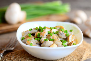 Fried mushrooms slices with sour cream sauce and young green onions in a bowl. Delicious mushroom recipe. Vintage wooden background. Country style. Closeup