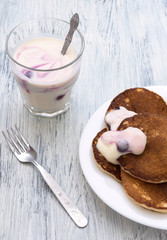 Pancakes with berry yoghurt in a white bowl on a wooden table. Yogurt with currants in the glass.