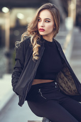 Beautiful young girl wearing black jacket sitting in the street.