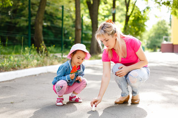 Fototapeta premium Mother is teaching her cute daughter to draw with chalk on sidewalk