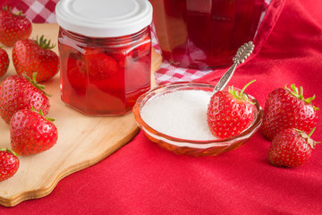 Homemade strawberry jam in the glass jar. Red, fresh berries and bowl of sugar on the table in the kitchen. Tasty, sweet food preparation for wintertime.