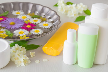 Metallic water bowl with daisy flowers for face, hands or feet washing. Cream and lotion bottles for body. Skin beauty care. Fresh jasmine flowers for fragrant atmosphere.